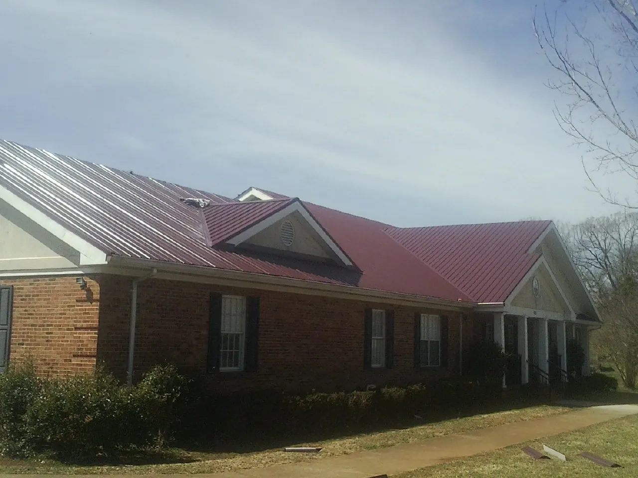 Red metal roof with gabled entries on a long brick building, from a Hail Damage Roof Repair job in Colrain