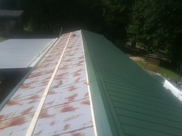 Old rusted panels beside newly installed green metal roofing — Wind Damage Roof Repair by Roofing Brothers in Colrain
