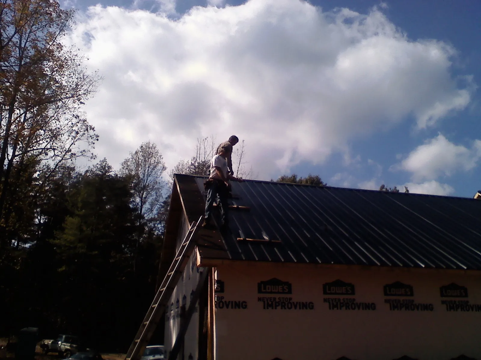 Roofer fastening dark metal panels high against a cloudy sky, from a Roof Inspection job in Colrain