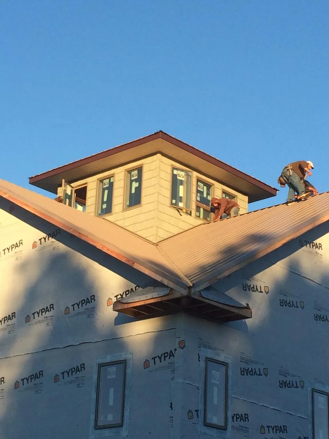 Roofers working around a rooftop cupola on a new metal roof at sunset — Roof Waterproofing in Colrain by Roofing Brothers